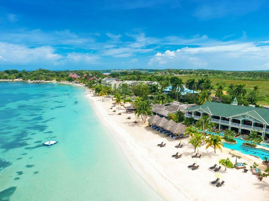Aerial view of a palm-lined beach resort beside turquoise water